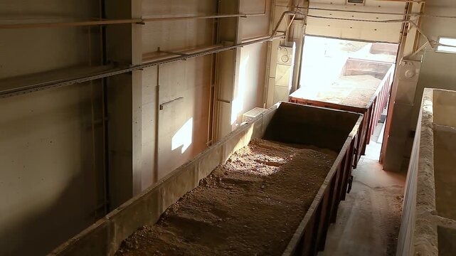 Open-top railcars loaded with clay and sand pull into the industrial bulk materials warehouse. Unloading of bulk materials (clay) at the industrial warehouse of a ceramic tile factory.