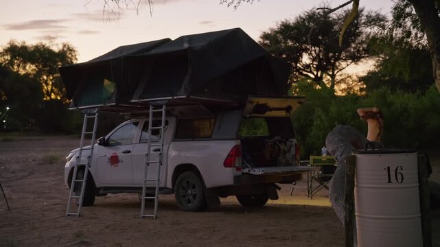 Adventurous traveler setting up rooftop tent on pickup truck during african safari expedition in namibian desert at sunset, cozy campsite