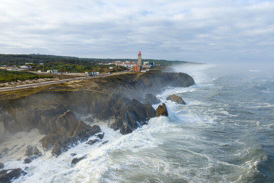 Aerial view of Farol Penedo da Saudade lighthouse standing on rugged cliffs with crashing waves and coastal mist Marinha Grande, Leiria, Portugal.