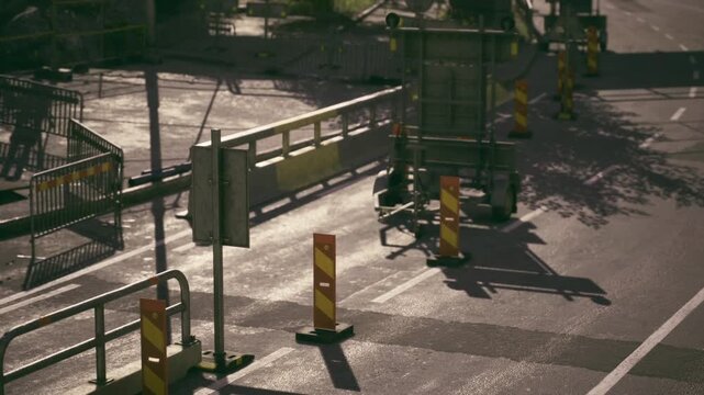 Daylight pours over a busy urban construction site where barriers guard freshly paved asphalt. Safety tools and machinery stand still, suggesting a pause in activity.