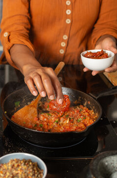 Close up hand adding sun dried tomatoes to pan sauce on stove