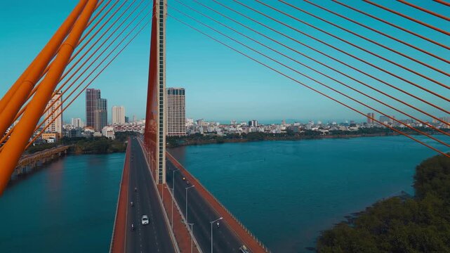aerial drone view of suspension cable bridge over Han river in Danang, geometric cable-stayed bridge architecture with modern city skyline and roadway, Da Nang Vietnam 4k