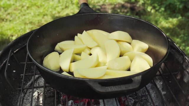 Cast Iron Skillet Filled With Potatoes Over Hot Embers, Rustic Outdoor Cooking Scene With Cast Iron Skillet Of Potatoes Over Burning Coals In Daylight