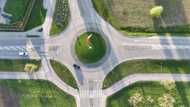 Top down drone shot of a modern circular roundabout intersection on a sunny day. Several cars driving through the roundabout, Austrian flag waving in the center. Clear road markings
