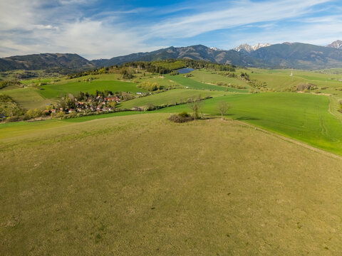 Aerial view of rolling green hills and a small village with the Tatra mountains in the background under a blue sky Liptovsky Trnovec, Zilina Region, Slovakia.