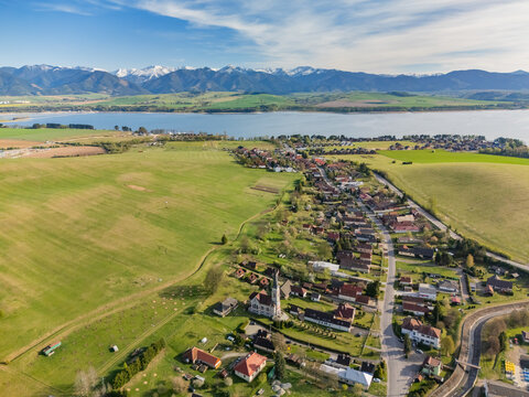Aerial view of Liptovsky Trnovec village with its church tower, green fields, and Liptovska Mara reservoir under the Tatra Mountains Liptovsky Trnovec, Zilina Region, Slovakia.