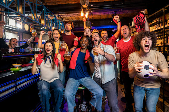 Happy friends watching soccer game and cheering in pub