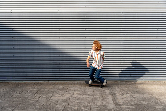 Urban skater cruising by corrugated metal wall in light