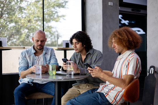 Three friends using smart phones at a cafe table indoors