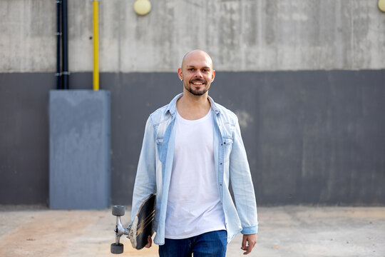 Urban skater holding skateboard by concrete wall outdoors