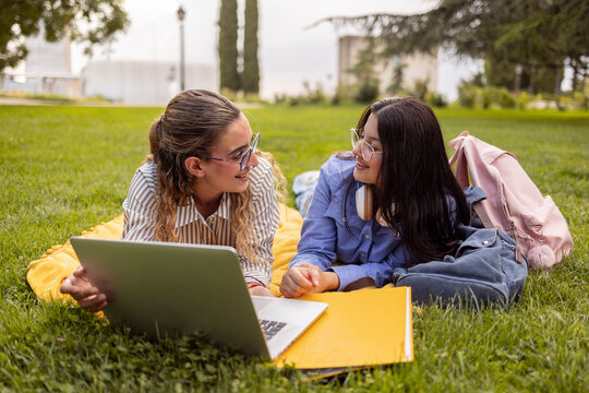 Two female students study together on campus lawn with laptop