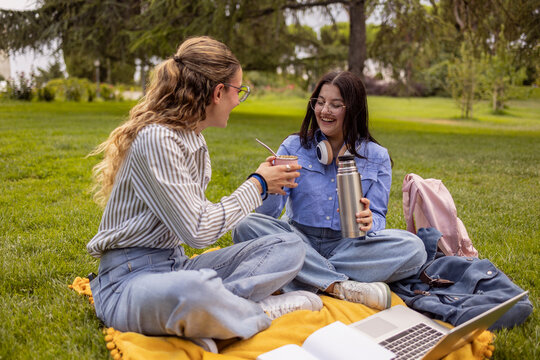 Two female students sharing mate on campus lawn break
