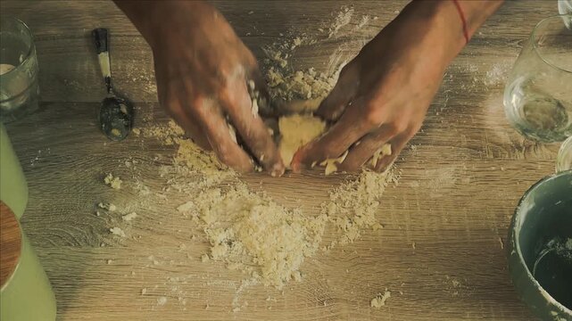Experienced male baker kneading homemade bread dough with flour on a dark rustic wooden table.