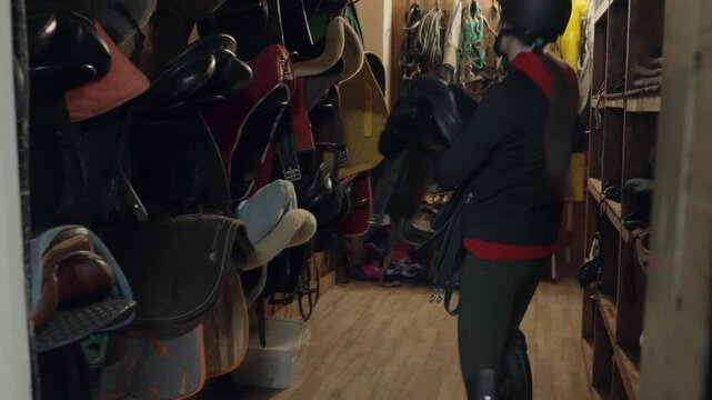 The girl takes the saddle for the horse. To go to a show jumping training. High quality 4k footage