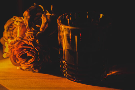 glass of whiskey by candlelight with flowers in the background, dim light