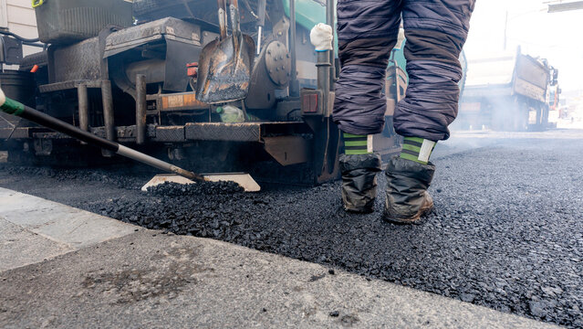 Workers paving street with asphalt machinery