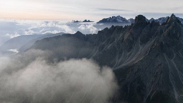 Aerial view of the jagged peaks of the Cadini group rising above a thick layer of clouds and mist in Auronzo di Cadore, Veneto, Italy.