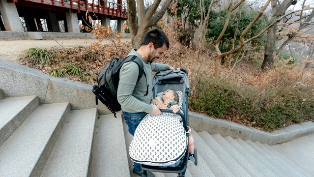 Father with backpack pushing stroller down park stairs
