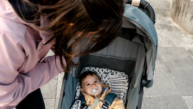 Woman adjusting baby stroller on city sidewalk outdoors