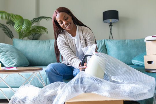 Black woman unboxing secondhand purchase in living room