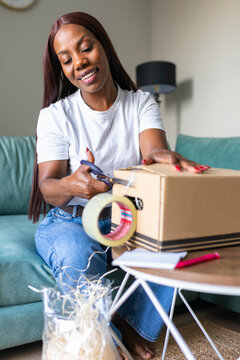 Black woman packing parcel for secondhand app sale at home