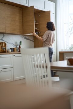 Woman Opening Wooden Cabinet in Modern White Kitchen