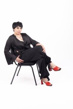 Woman sitting on chair while posing in black clothes for portrait in professiona