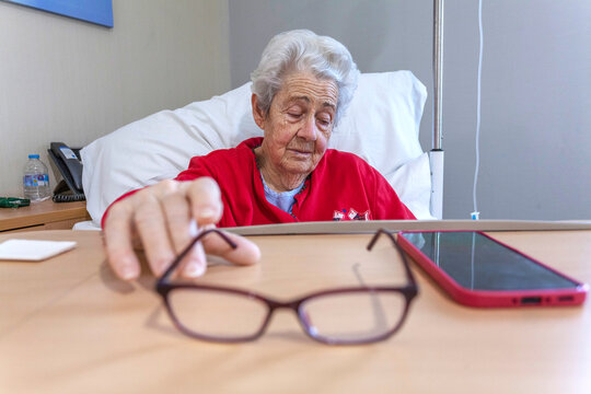 Elderly patient in hospital bed reaching for glasses