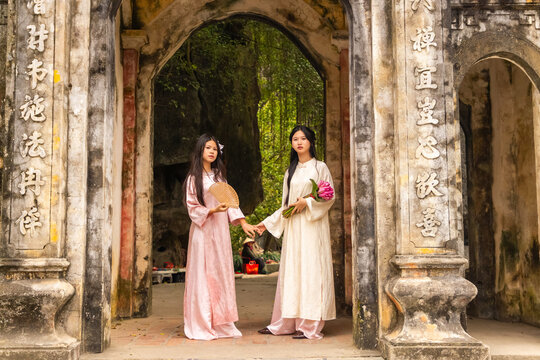 Young Vietnamese teenagers standing in ao dai by ancient temple gate