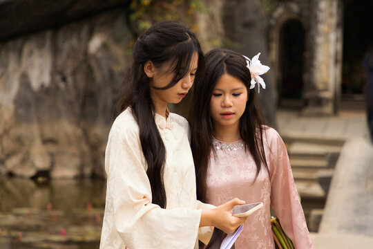 Young Vietnamese teenagers in ao dai using phones by ancient temple