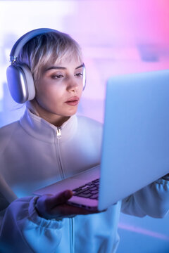 Futuristic woman using laptop with headphones in neon light