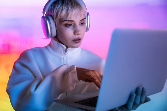 Futuristic woman in headphones using laptop in neon light