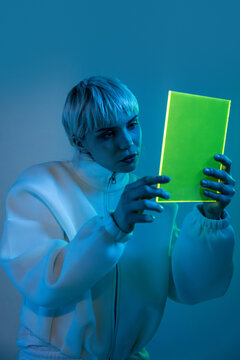 Futuristic woman examining glowing tablet in blue light