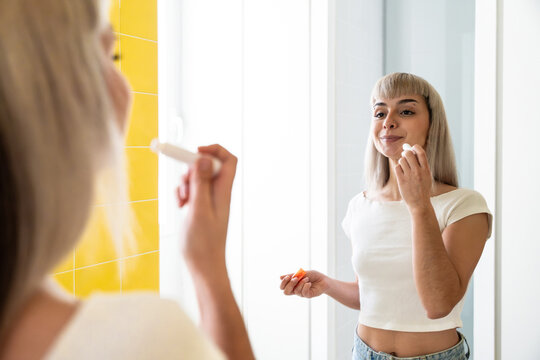Young woman applying lipstick in mirror at home bathroom
