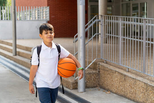 Young student holding basketball at school entrance