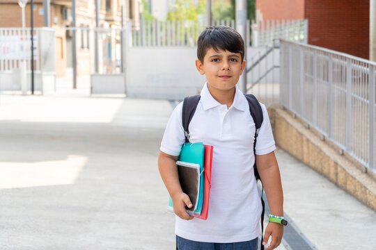 Young boy holding school supplies outside the building