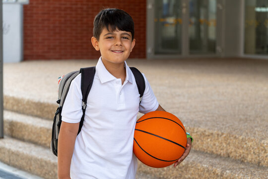 Young student with backpack and basketball at school