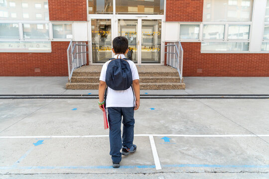 Boy entering school with backpack and book