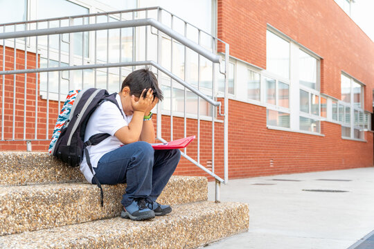 Stressed boy sitting alone outside school building