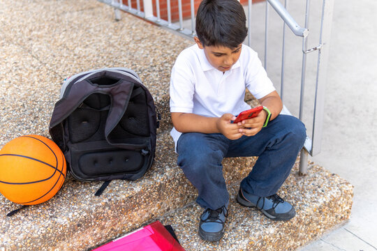 Boy sitting on steps with smartphone at school