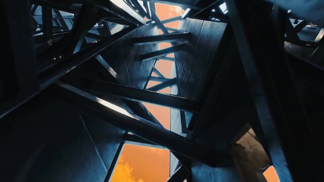Tilting camera revealing vertical steel shaft interior, showing cross-bracing and orange sky