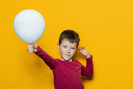 Boy holding white balloon against bright yellow background