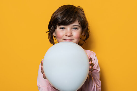 Smiling girl holding white balloon on yellow background