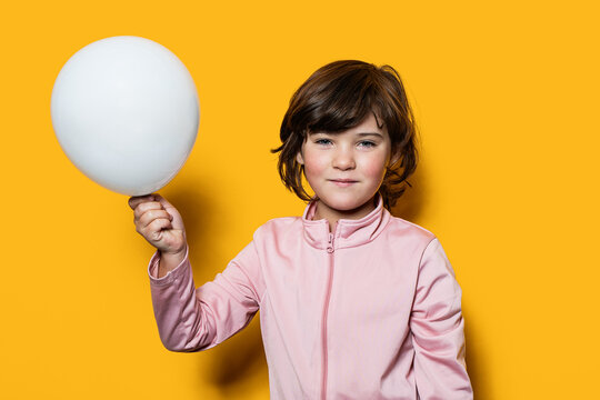 Young child holding white balloon against yellow background