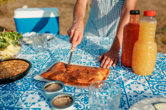 Woman cutting empanada on summer picnic table with drinks