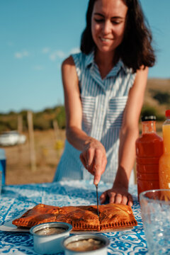 Woman cutting empanada at summer picnic with tuna cans