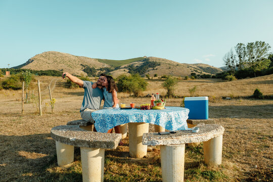 Couple taking a summer picnic selfie at countryside table