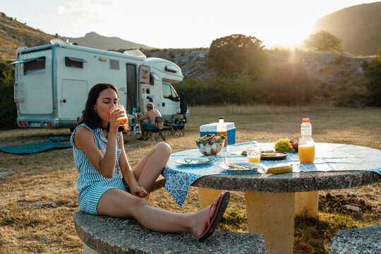 Woman enjoying summer picnic drink at campsite sunset