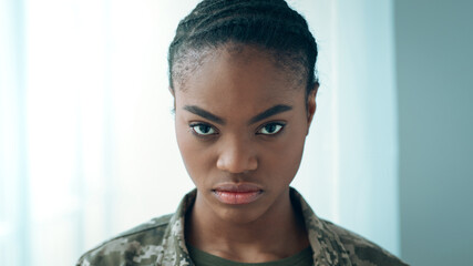 Naklejka premium A military personnel looks directly at the camera with focus and determination. The background is simple and light, emphasizing the subject's expression and uniform. The atmosphere suggests readiness.