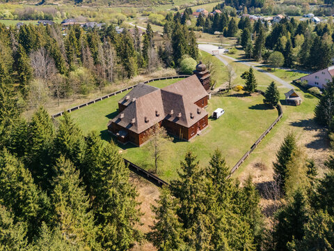 Aerial view of the Wooden Articular Church of Svaty Kriz surrounded by a wooden fence and dense pine forest under a clear sky in Svaty Kriz, Zilinsky kraj, Slovakia.